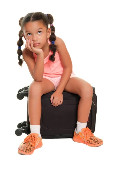 Kleines Mädchen, das gelangweilt und ungeduldig auf einem Koffer sitzt - isoliert auf weiß — Stockfoto