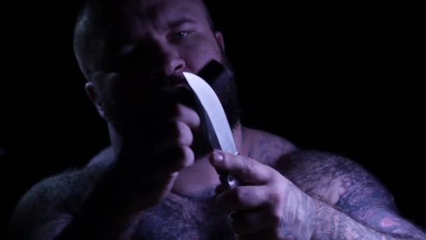 Лисий татуйований бородатий м'язовий гангстер з ножем і точилкою. 4K UHD — стокове відео