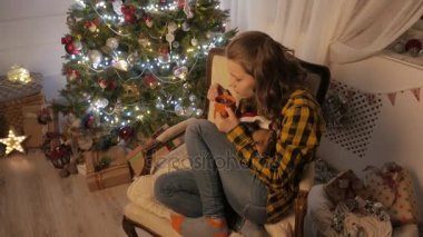 Genç kız gülümseyerek ve bir fincan çay içme. Noel ağacı ve tatil ruh hali. 4k Uhd.