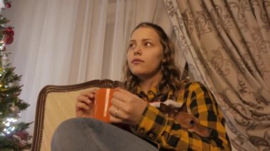 Genç kız gülümseyerek ve bir fincan çay içme. Noel ağacı ve tatil ruh hali. 4k Uhd.