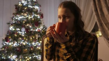 Genç kız gülümseyerek ve bir fincan çay içme. Noel ağacı ve tatil ruh hali. 4k Uhd.