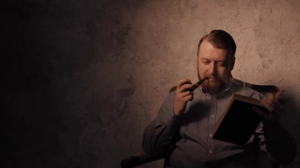男は、暗い部屋と禁煙パイプで本を読みます。4 k Uhd — ストック動画