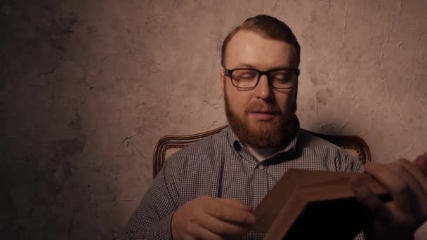 L'uomo legge un libro in una stanza buia e fuma la pipa. 4K UHD — Video Stock