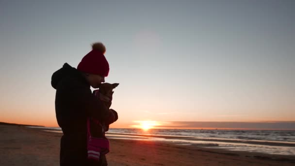 Kvinna leker med sin hund vid solnedgången nära Östersjön — Stockvideo