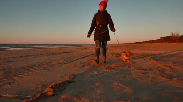 Mujer corriendo, paseando, jugando y divirtiéndose con su perrito al atardecer en una playa cerca del mar Báltico en primavera. Paisaje colorido . — Vídeos de Stock