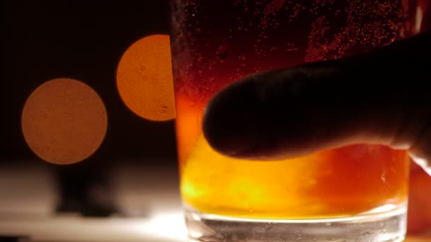 Cocktail de cor escura com gelo. Tiro de perto num fundo desfocado. Mão a abanar . — Vídeo de Stock