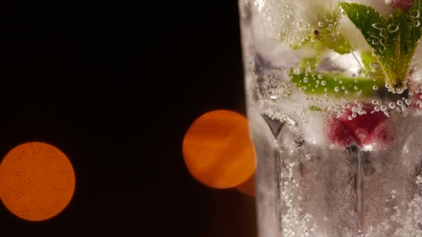 Склянка з напоєм, льодом, м'ятою та ягодами на розмитому фоні — стокове відео