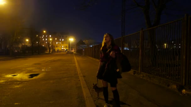 Chica adolescente con un perrito en una calle nocturna . — Vídeo de stock