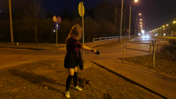 Chica adolescente con un perrito en una calle nocturna . — Vídeo de stock