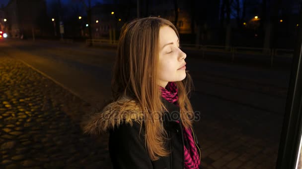 Retrato de una linda chica adolescente sonriente pensativa en una calle nocturna de la ciudad. Mirando la cartelera — Vídeo de stock