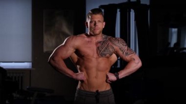 Genç vücut geliştirmeci bir spor salonunda poz çıplak bir gövde ile. 60-24fps 4k