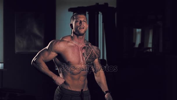Junger Bodybuilder mit nacktem Oberkörper posiert in einem Fitnessstudio. 60 bis 24fps 4k — Stockvideo