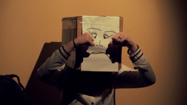 Chica de noche vistiendo una caja con una cara infeliz dibujando en su cabeza. Concepto de dolor e infelicidad. 4K UHD 60 a 24fps — Vídeos de Stock