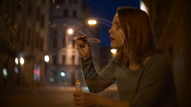 Portréja egy aranyos mosolygós tini lány, egy éjszakai város szappanbuborék fújás utcában — Stock videók