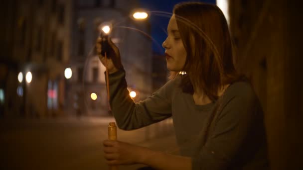 Portrait d'une jolie adolescente souriante sur une rue nocturne soufflant des bulles de savon — Video