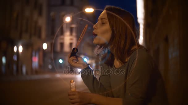 Porträtt av en söt leende tonåring flicka på en natt stadsgata blåser såpbubblor — Stockvideo