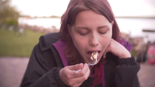 Молода дівчина їсть торт на відкритому повітрі — стокове відео