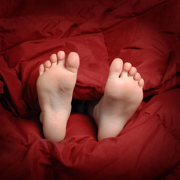 Nogi w łóżku z czerwony koc odpoczynku — Zdjęcie stockowe