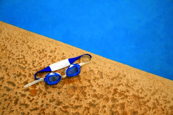 Gafas de natación junto a la piscina con agua azul — Foto de Stock