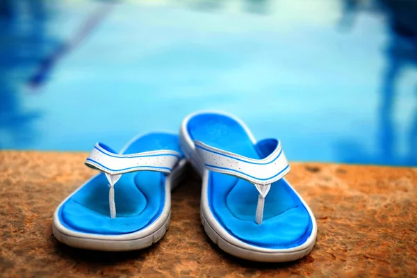 Sandálias chinelos ao lado de piscina clara água azul — Fotografia de Stock