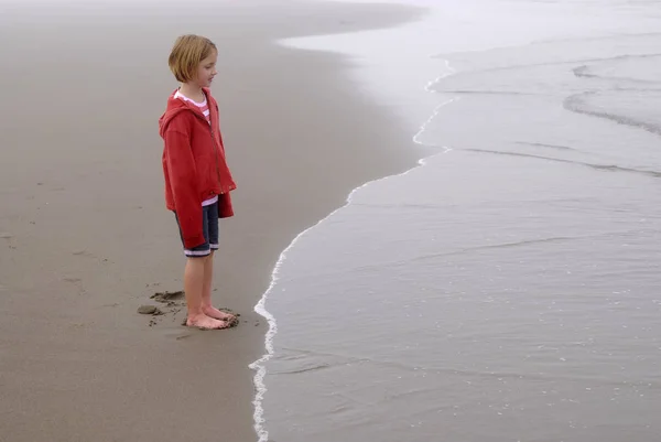 Gadis kecil di pantai berkabut Mengenakan jaket merah — Stok Foto