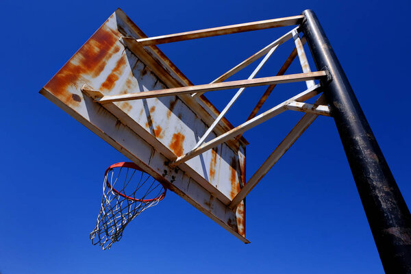 Rusted rusty old metal basketball hoop outside against a blue sky on playground