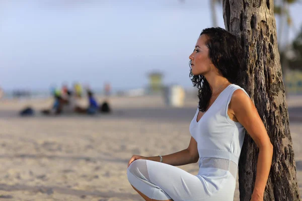 Vrouw, gehurkt op een boom in het strand — Stockfoto