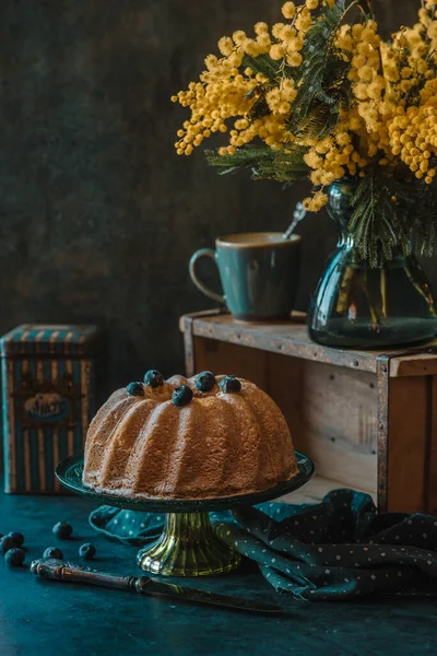 Delicious honey cake with blueberries and a branch of mimosa on a rustic background