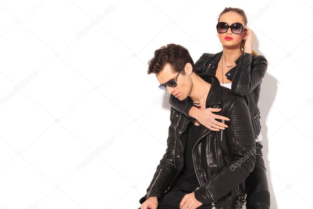 woman in leather jacket embracing seated man from behind 