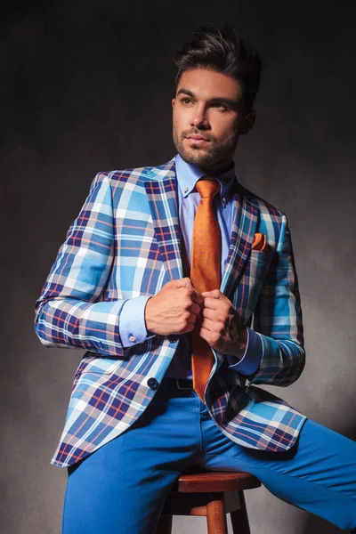 Seated young man in checkered suit holding his collar — Stock Photo, Image
