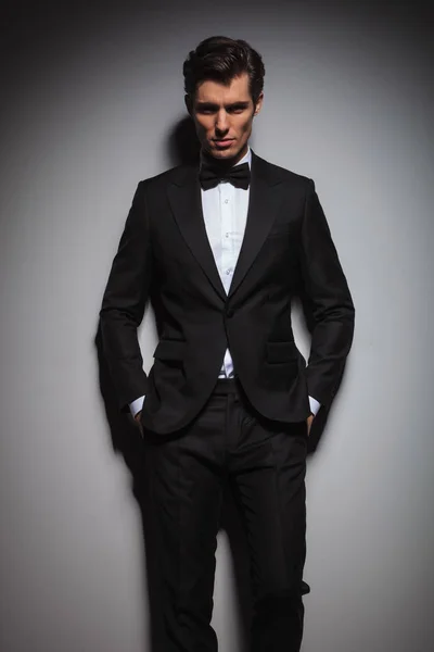 Poważny człowiek młody, noszenie tuxedo stoi z rąk w kieszeniach — Zdjęcie stockowe