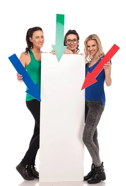 Drei junge Frauen, die Pfeile auf ein großes leeres Brett zeigen — Stockfoto