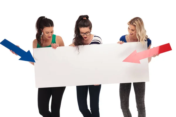 Three amazed women pointing arrows to a big blank board — Stock Photo, Image