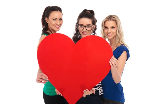 Três mulheres casuais sorridentes segurando um grande coração vermelho — Fotografia de Stock