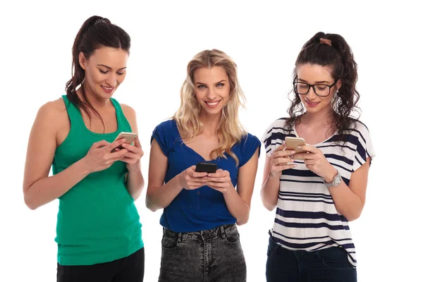 Drie gelukkige casual vrouwen chat op hun telefoons — Stockfoto