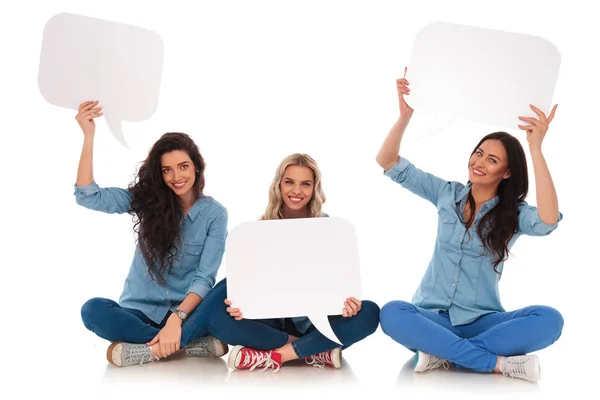 Tres mujeres jóvenes sentadas sonríen y sostienen burbujas en blanco — Foto de Stock