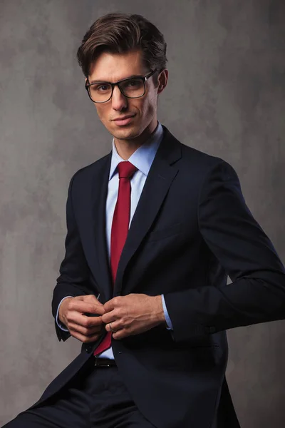 Sonriente joven hombre de negocios sentado abotonando su traje — Foto de Stock