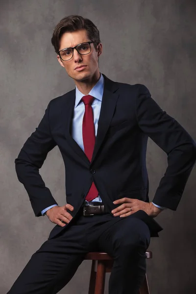 Serious young business man with hands on waist sitting — Stock Photo, Image