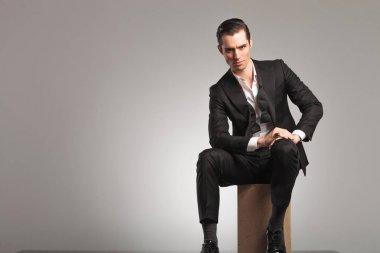 elegant man sitting on wooden box with undone bowtie clipart