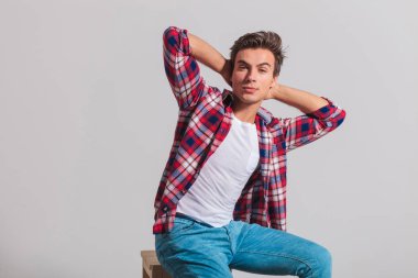 young casual man sitting and holding his hands behind head