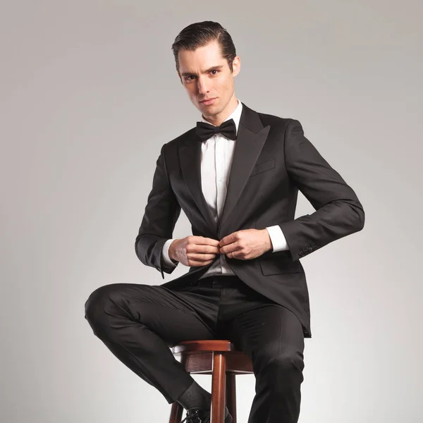 Elegancki mężczyzna w smokingu guziki jego płaszcz siedząc — Zdjęcie stockowe