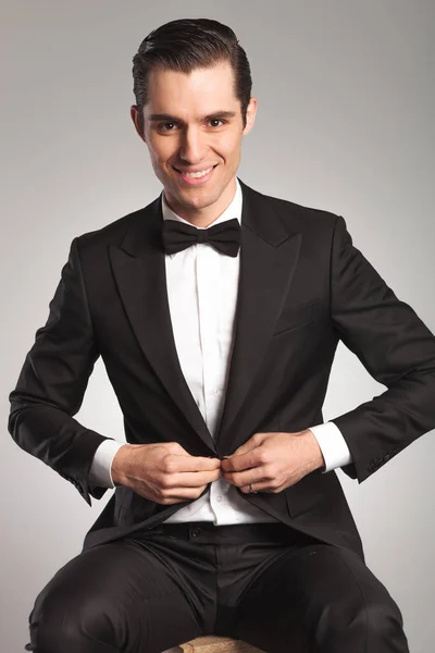 Young elegant man unbuttoning his tuxedo while sitting — Stock Photo, Image