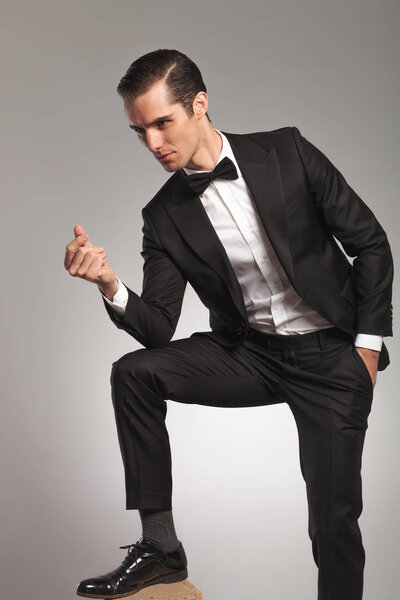 бизнесмен в смокинге щёлкает пальцем и смотрит в сторону
