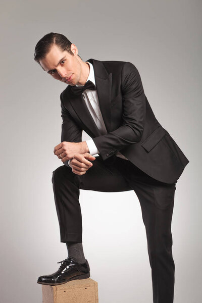 Человек в смокинге лежит с поднятой ногой на деревянной коробке
