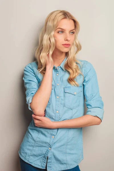 Blonde woman holding hand on neck and looks to side — Stock Photo, Image