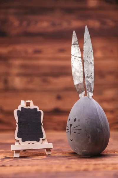 Huevo de Pascua gris con orejas de conejo cerca de tablero en blanco — Foto de Stock