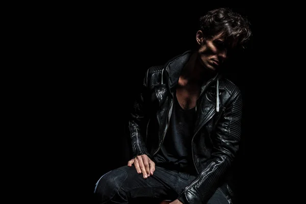 seated fashion model wearing leather jacket and looking away