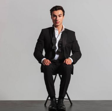 takım elbise ve geri alınan papyon sandalyede oturan zarif adam