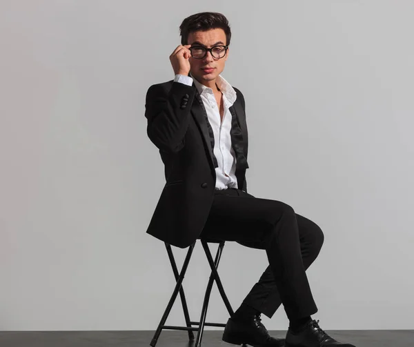 Elegant man in tuxedo and undone bowtie fixing his glasses — Stock Photo, Image