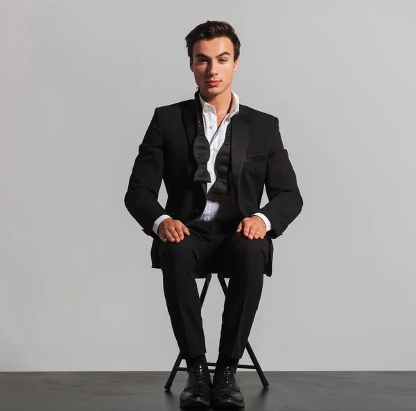 Homem elegante em terno e desfeito bowtie sentado na cadeira — Fotografia de Stock